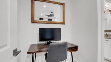 Een moderne kamer met een houten bureau, een zwart beeldscherm, een grijze stoel en een plafondventilator.