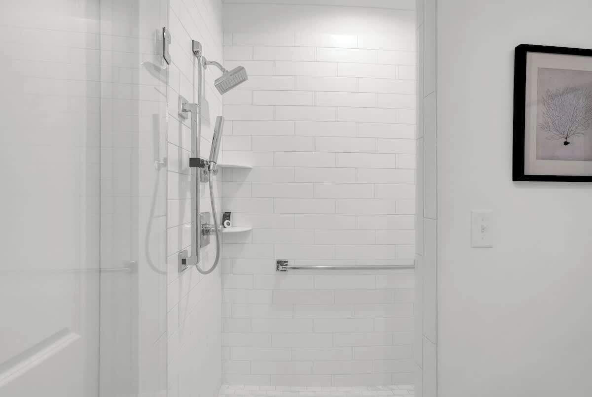 Ein modernes Badezimmer mit weißen Fliesen, einer Glasdusche, einem gerahmten Kunstwerk an der Wand und einem Handtuchhalter.