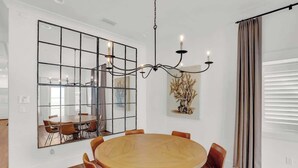 A modern dining room with a round wooden table, six chairs, a chandelier, a large mirror, and a decorative plant. - Church St Collection - Suite 16 (Fairhope)