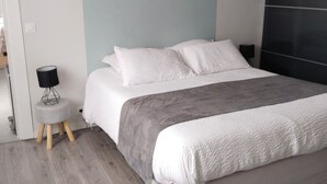 Une chambre moderne avec un grand lit, une literie aux tons de gris et de blanc, un mur d’accent gris et une petite table de chevet avec une lampe.