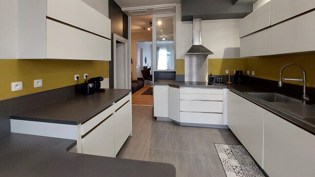 Une cuisine moderne avec des armoires blanches, un îlot central et une hotte de cuisinière en acier inoxydable.