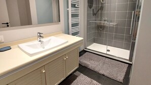 Une salle de bain moderne avec un meuble-lavabo à deux vasques, un grand miroir, une douche à parois de verre et deux petits tapis sur le sol.