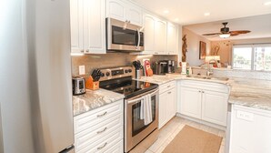 A modern kitchen with white cabinets, stainless steel appliances, a microwave, stove, and a ceiling fan. - New to Rental Program! Beautiful Ocean View 3/2 at St. Augustine Beach & Tennis Club 301 (St. Augustine)