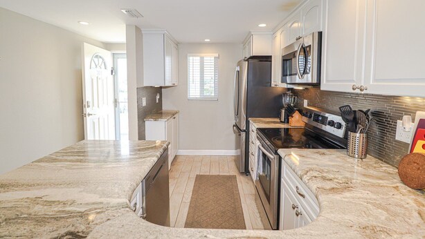 A modern kitchen with granite countertops, stainless steel appliances, and white cabinetry. - New to Rental Program! Beautiful Ocean View 3/2 at St. Augustine Beach & Tennis Club 301 (St. Augustine)