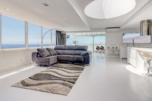 Un salon moderne avec un canapé d’angle, une grande moquette et une vue sur la ville grâce à de grandes fenêtres.