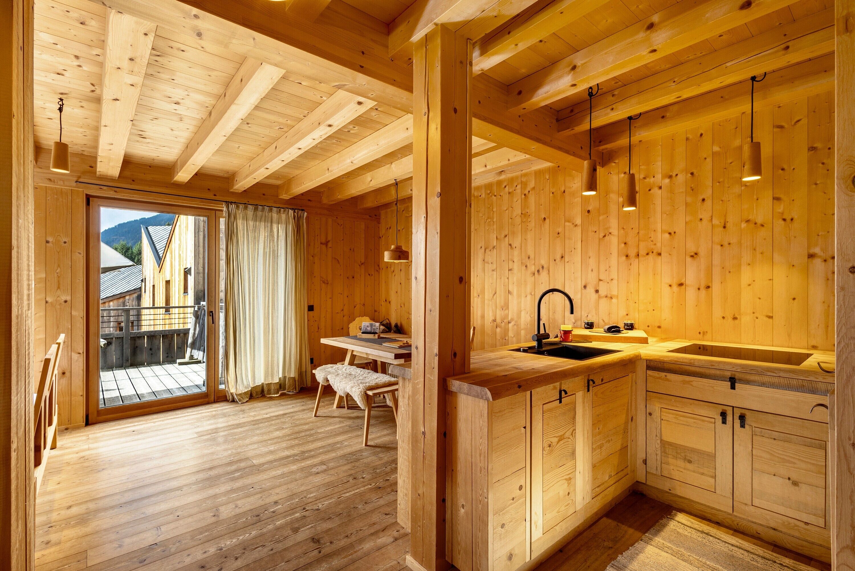 Un intérieur en bois comprenant une cuisine, un coin repas et des portes-fenêtres coulissantes donnant sur une terrasse extérieure.