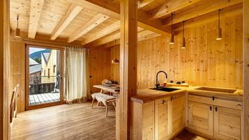 Un intérieur en bois comprenant une cuisine, un coin repas et des portes-fenêtres coulissantes donnant sur une terrasse extérieure.
