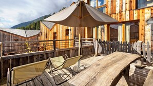 Une terrasse en bois avec une table et deux chaises, une clôture en bois et une chaîne de montagnes en arrière-plan.