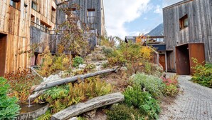 Un edificio moderno con paredes exteriores de madera, una pequeña fuente de agua y un jardín con diversas plantas.