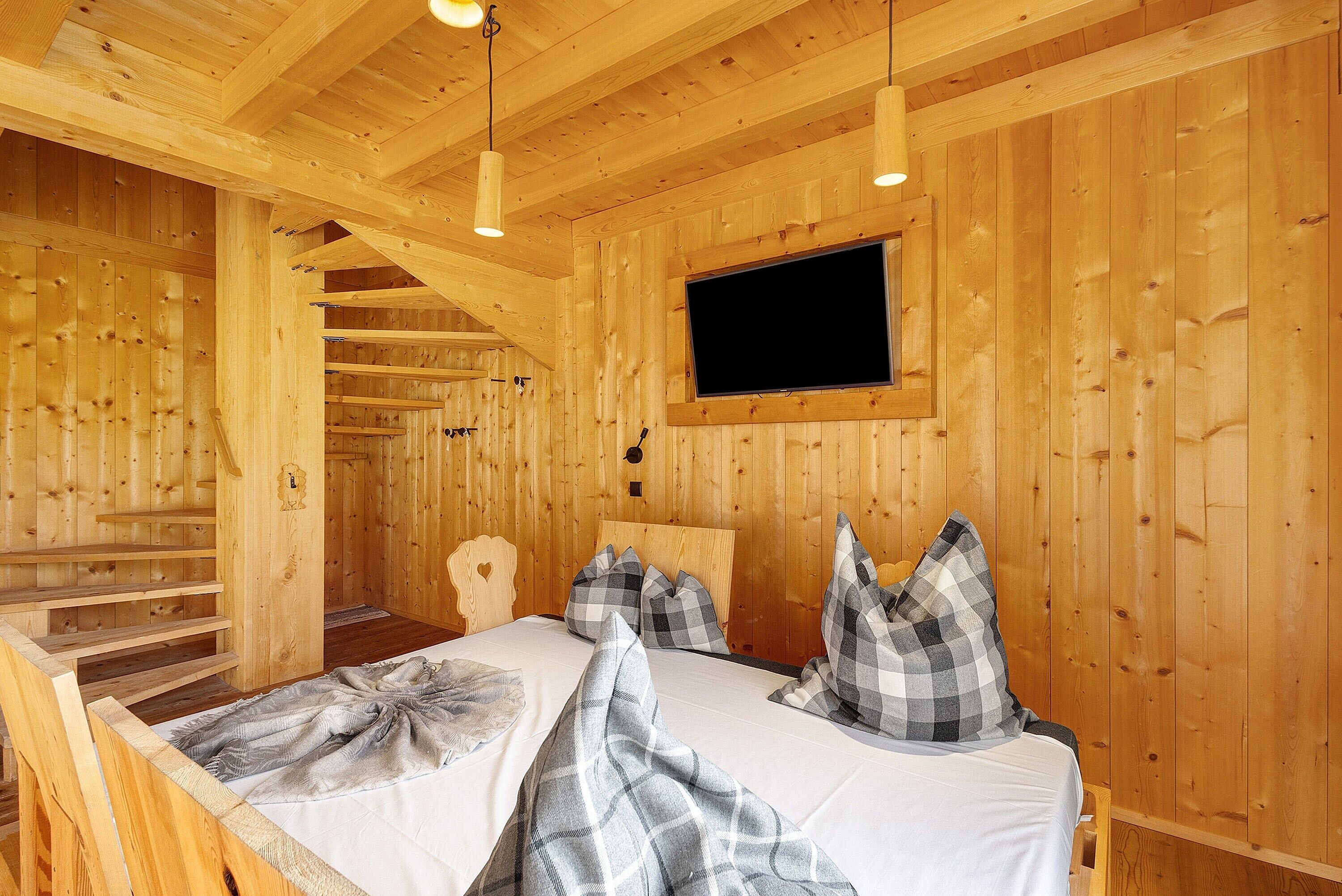 A wooden cabin interior with a bed, a television, and a staircase.