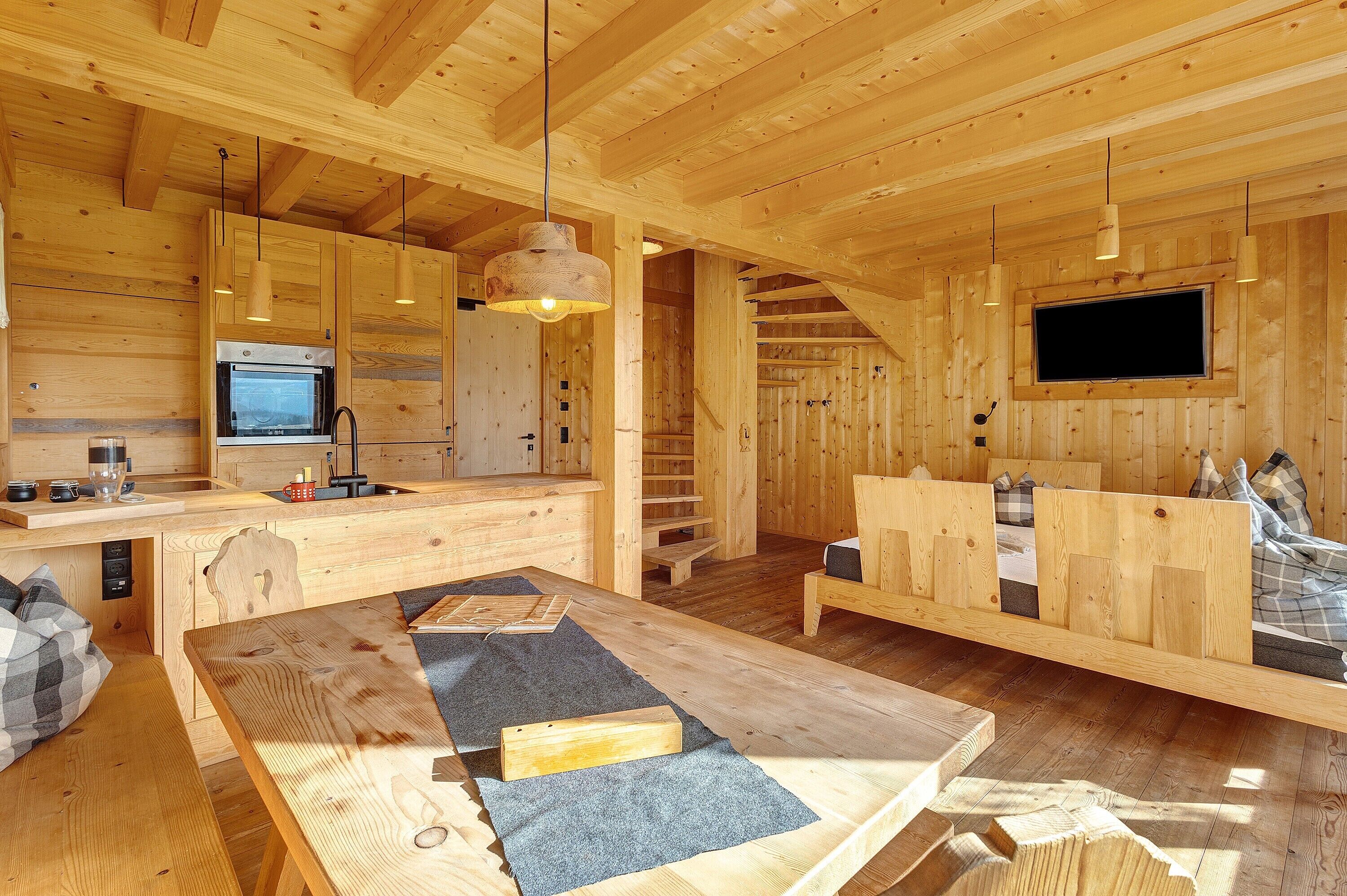 Interior de una cabaña de madera con cocina, comedor y zona de descanso.