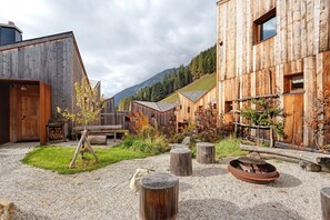 A rustic wooden building with a gravel courtyard, a small tree, and a fire pit.