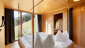 Una habitación de madera con una cama, ventanas amplias y vistas al exterior.