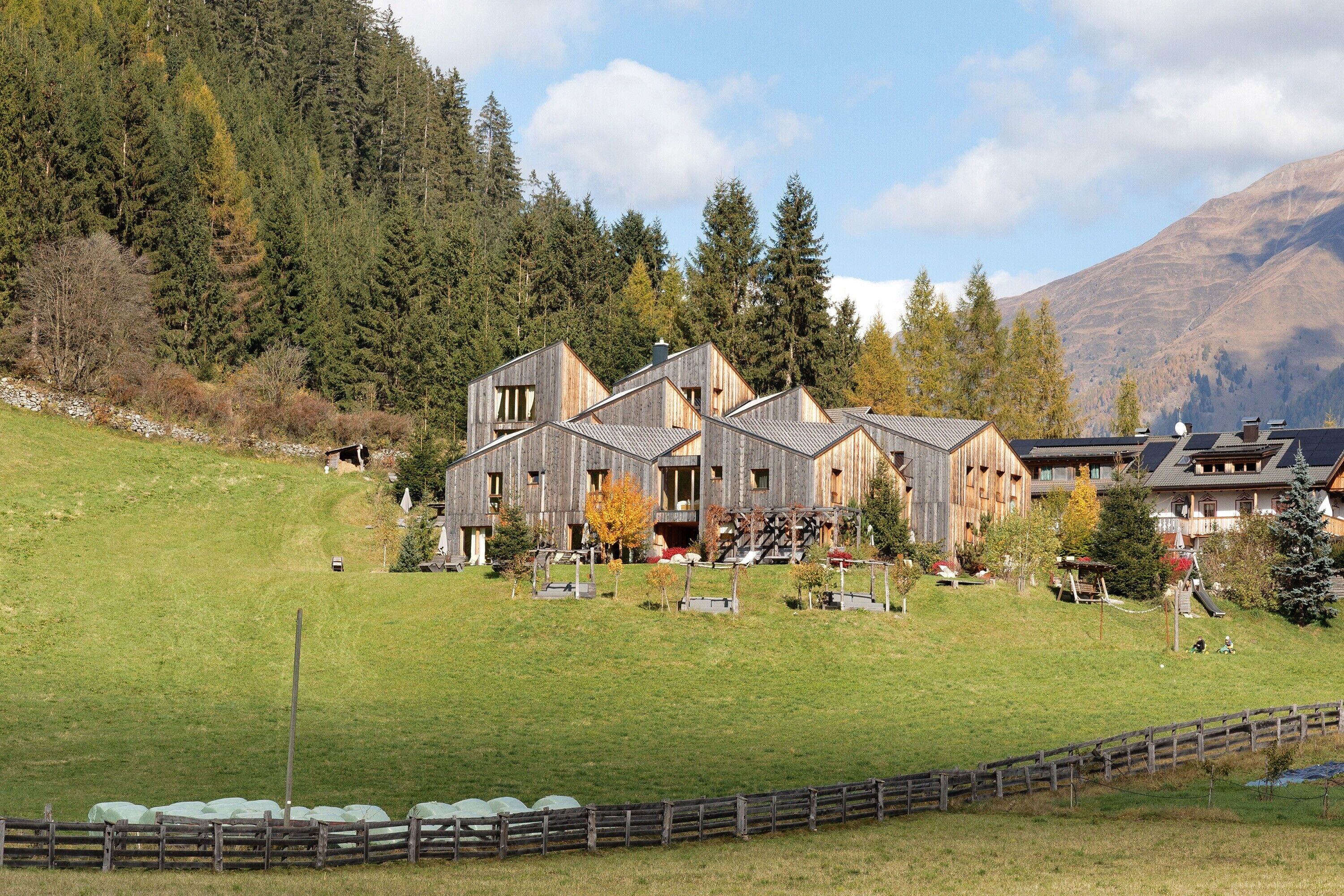 Ein holzgestütztes Chalet mit mehreren Ebenen, umgeben von einer grasbewachsenen Hügelkuppe und dichtem Wald.