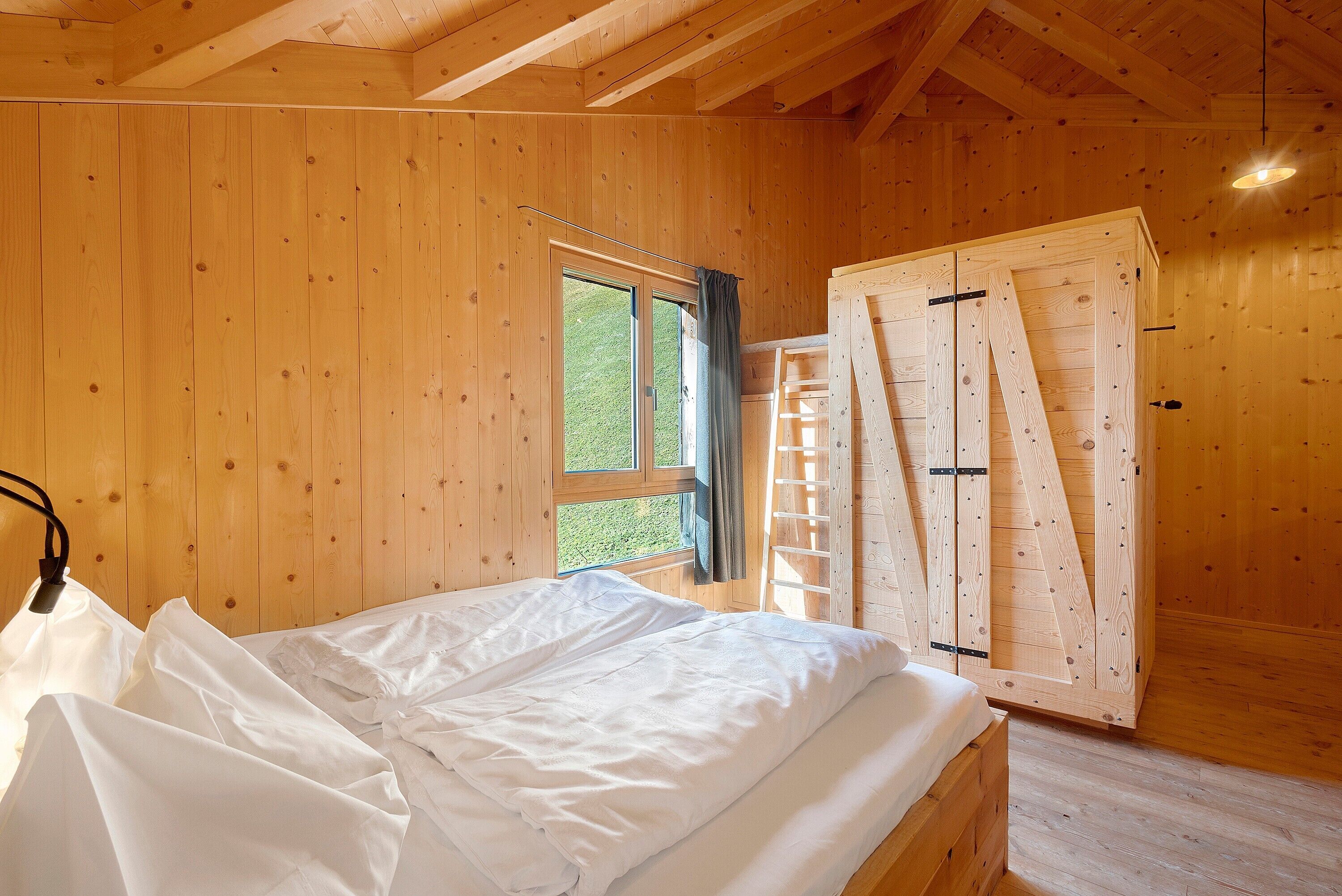 A wooden cabin room with a bed, a window, and a ladder.