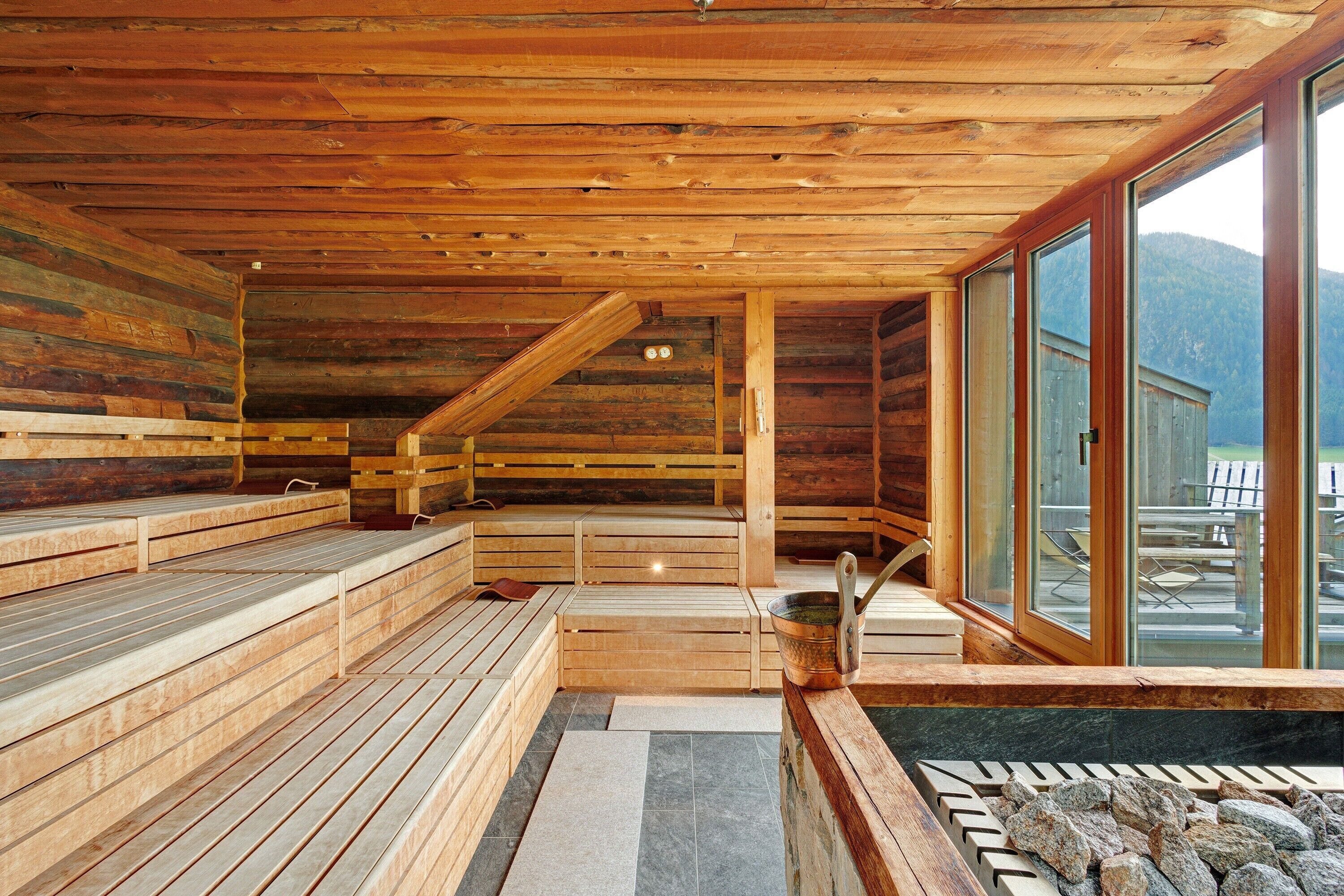A wooden sauna with benches, a stone hot tub, and large windows offering a mountain view.