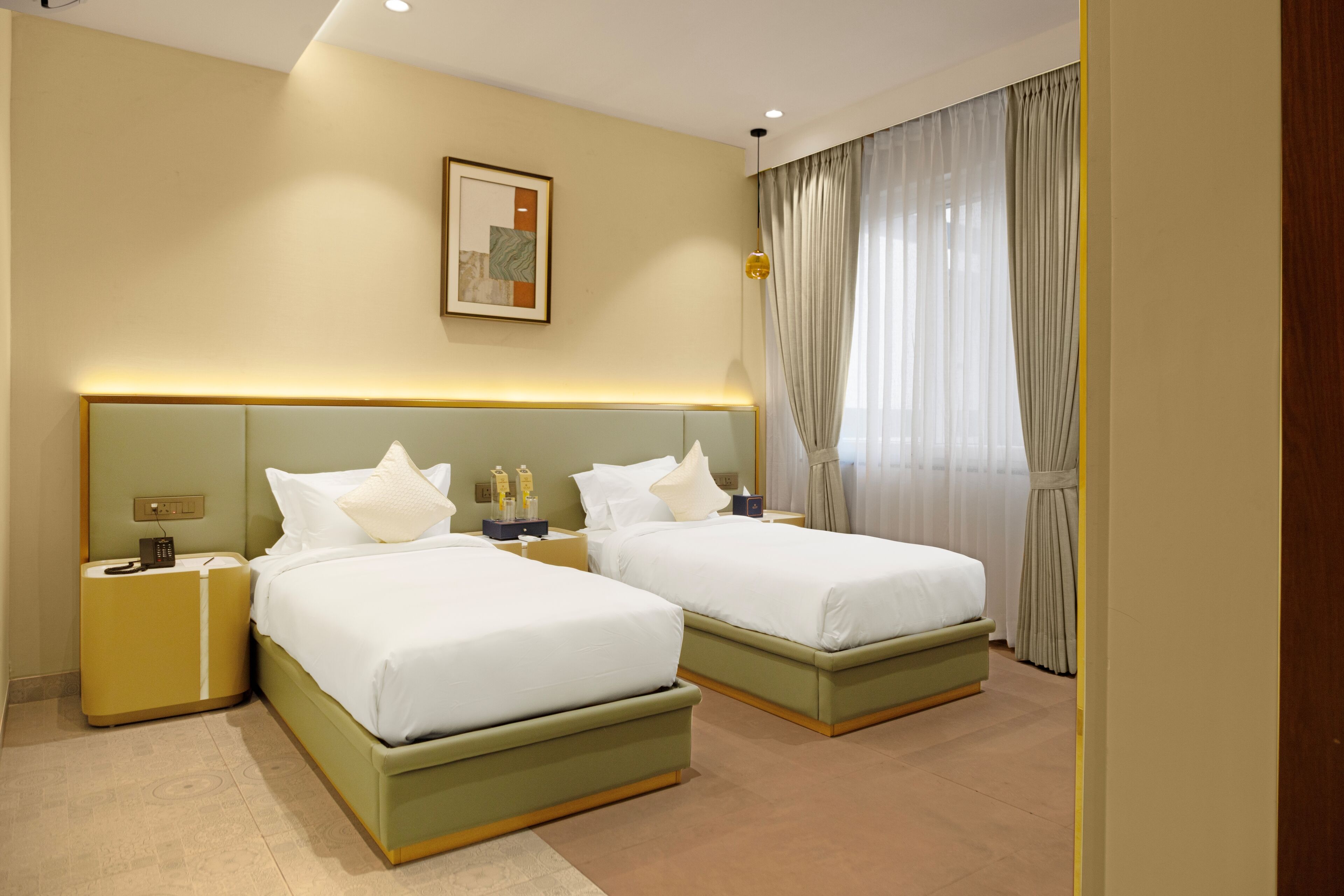 Habitación de hotel con dos camas, una mesita de noche, una lámpara, un cuadro en la pared y una ventana con cortinas.