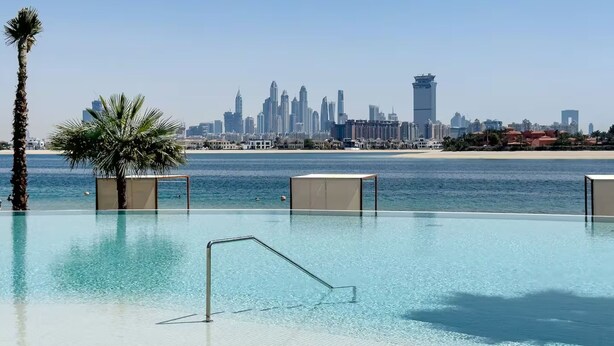 A pool with clear water, palm trees, and a city skyline in the background. - Ellington Beach House - Palm Jumeirah (Dubai)