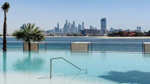 A pool with clear water, palm trees, and a city skyline in the background. - Ellington Beach House - Palm Jumeirah (Dubai)