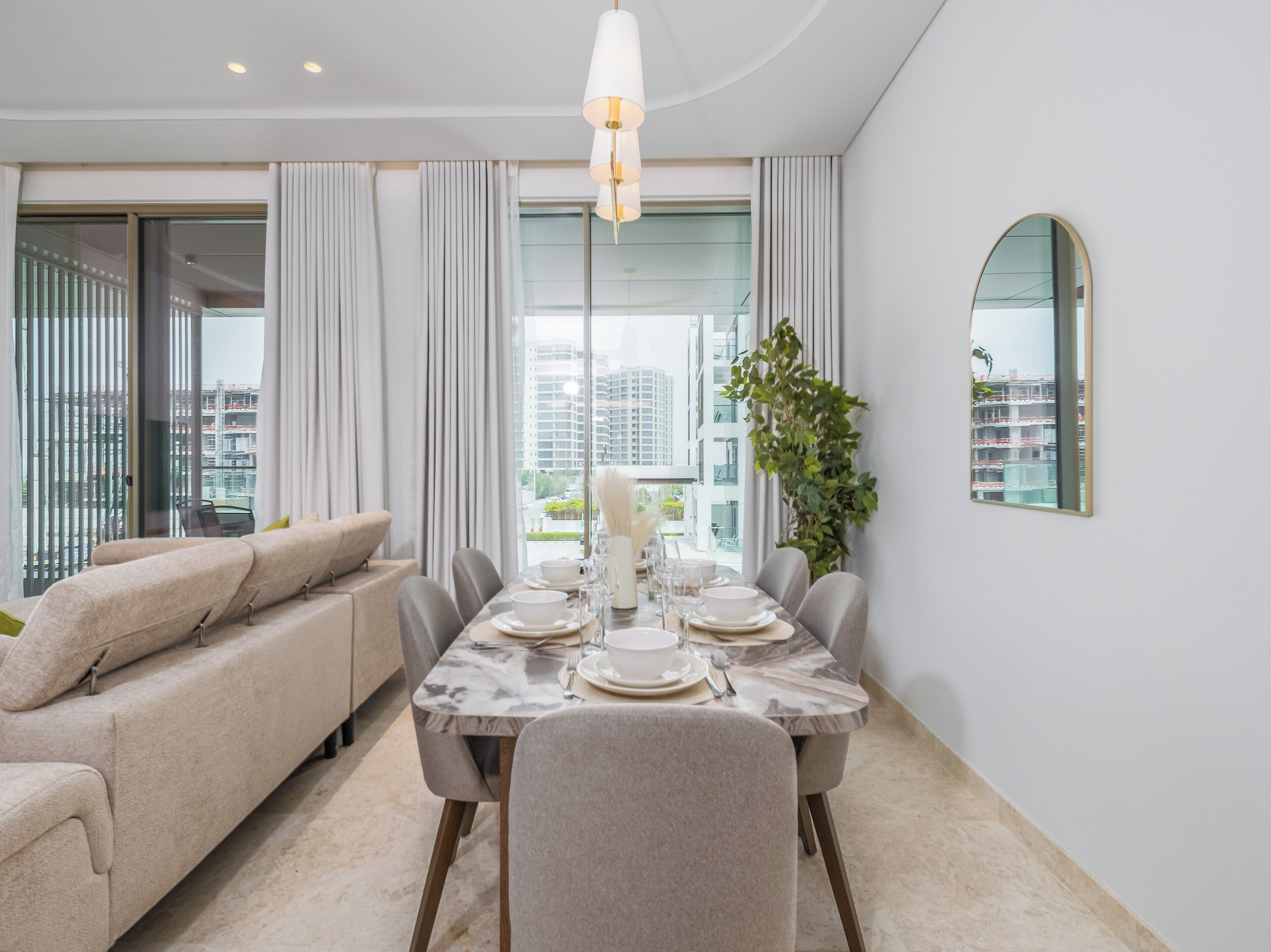 A modern dining area with a marble table, grey upholstered chairs, and a white chandelier.