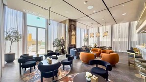 A spacious lobby with a mix of seating areas, including sofas and chairs, a coffee table, and a reception desk. Large windows provide natural light and a view of the cityscape. - Ellington Beach House - Palm Jumeirah (Dubai)