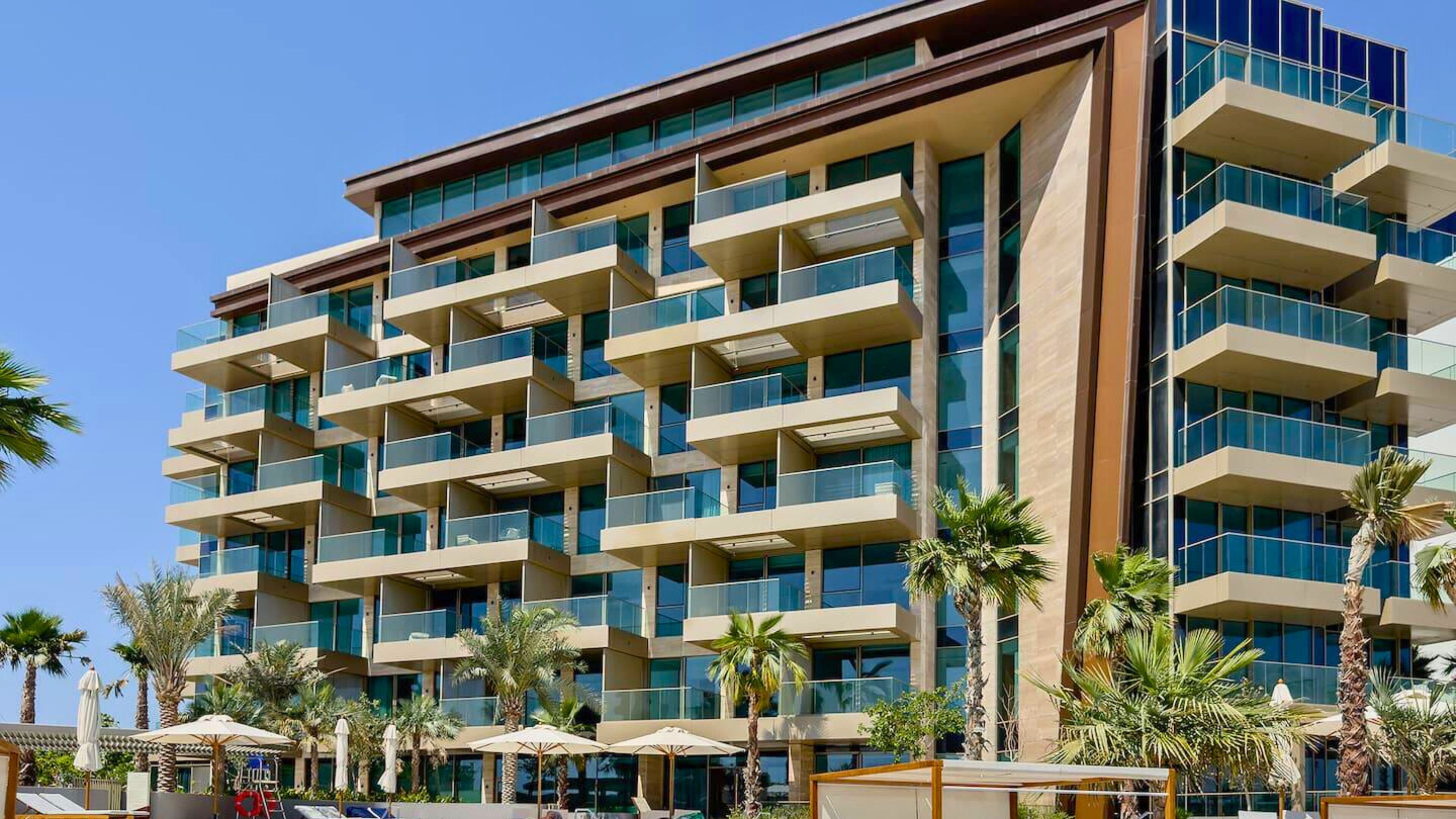 A multi-story hotel with balconies, palm trees, and outdoor seating areas.