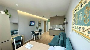 Ein modernes Hotelzimmer mit Bett, Schreibtisch, Sessel, Sofa, Fernseher und Küchenzeile.