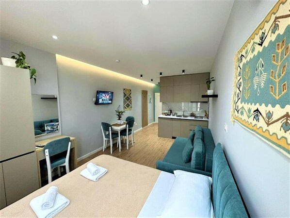 A modern hotel room with a bed, a desk, a chair, a sofa, a TV, and a kitchen area. - TreA Accomodations - Suite Lungomare (Vlorë)