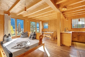A wooden cabin interior with a bed, dining table, and kitchen area.