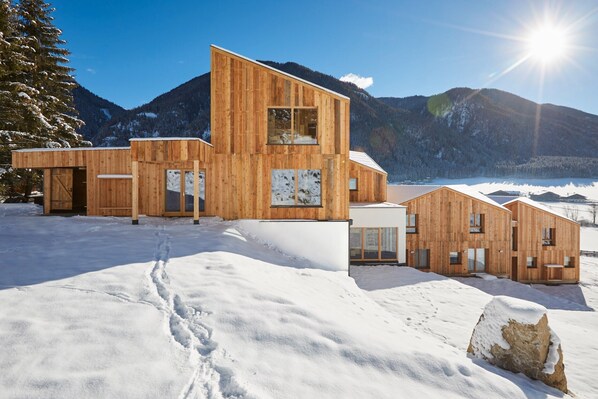 A wooden cabin with a large window, a door, and a snow-covered landscape.