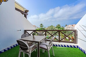 A balcony with a table and chairs, a view of palm trees and buildings, and artificial green turf.