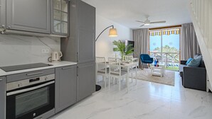 Une cuisine moderne avec des meubles gris, un four encastré et un coin repas avec des chaises et une table blanches.