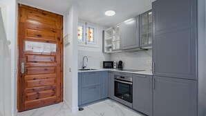 Une cuisine avec des meubles de couleur grise, une porte en bois, un four à micro-ondes, un four traditionnel et une fenêtre avec des vitraux.