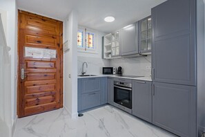 Eine Küche mit grauen Schränken, einer Holztür, einer Mikrowelle, einem Backofen und einem Fenster mit Buntglas.