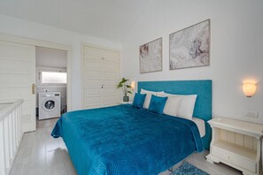 A bedroom with a large bed, a washing machine in the background, and two wall-mounted light fixtures.