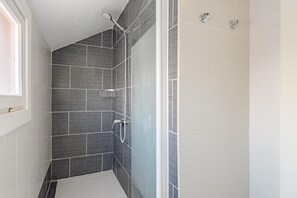 Ein modernes Badezimmer mit dunklen Fliesen, einer Dusche und einem Fenster.
