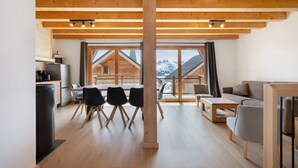 A modern interior with a wooden ceiling, a dining area with chairs, a sofa, and a kitchen area with appliances.