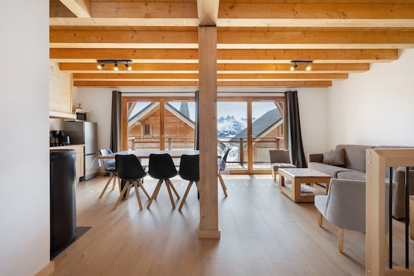 A modern interior with a wooden ceiling, a dining area with chairs, a sofa, and a kitchen area with appliances.