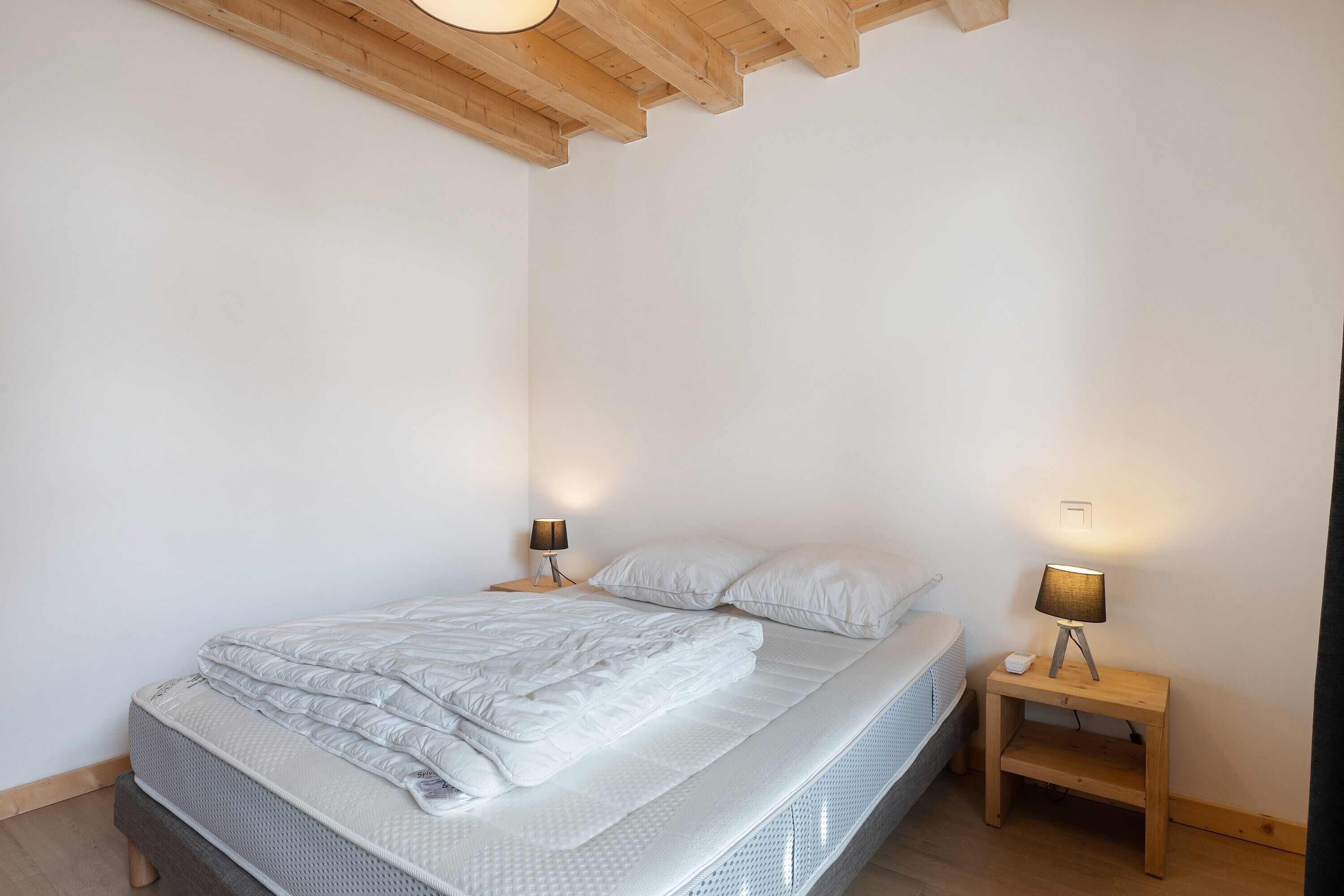 A bedroom with a bed, two bedside tables, a lamp on each table, and a wooden ceiling.