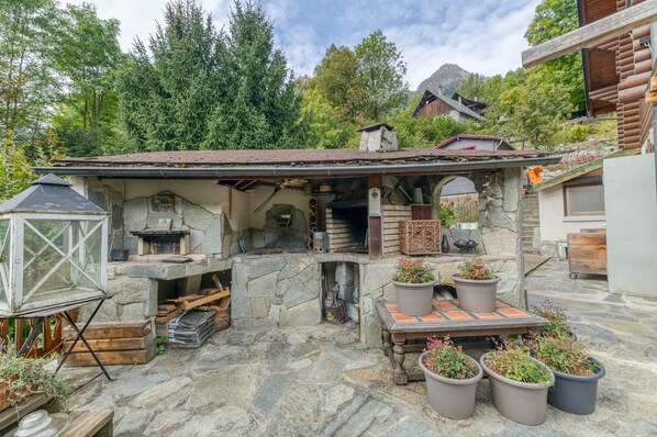 Un edificio rústico de piedra con chimenea de piedra, bancos de madera y plantas en macetas.