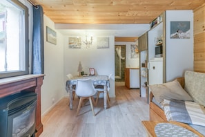A cozy room with a fireplace, a dining table with chairs, a sofa, and a kitchen area.