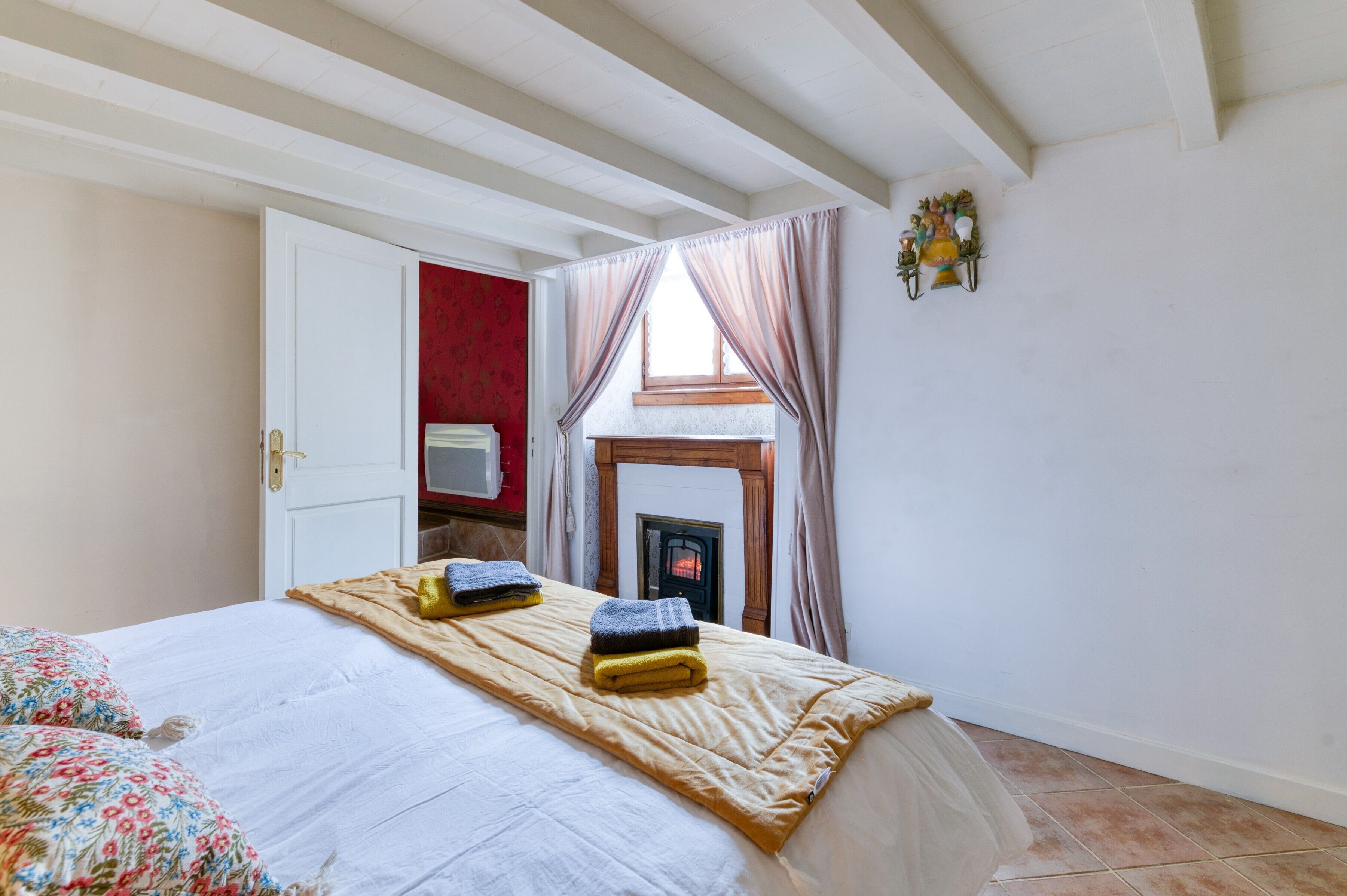 A bedroom with a bed, a red door, a fireplace, and a window with curtains.