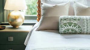 A neatly made bed with white linens and a decorative pillow, a bedside lamp, and a view of greenery outside a window. - Downham House: Spacious 4BR, Old Town ALX (Alexandria)