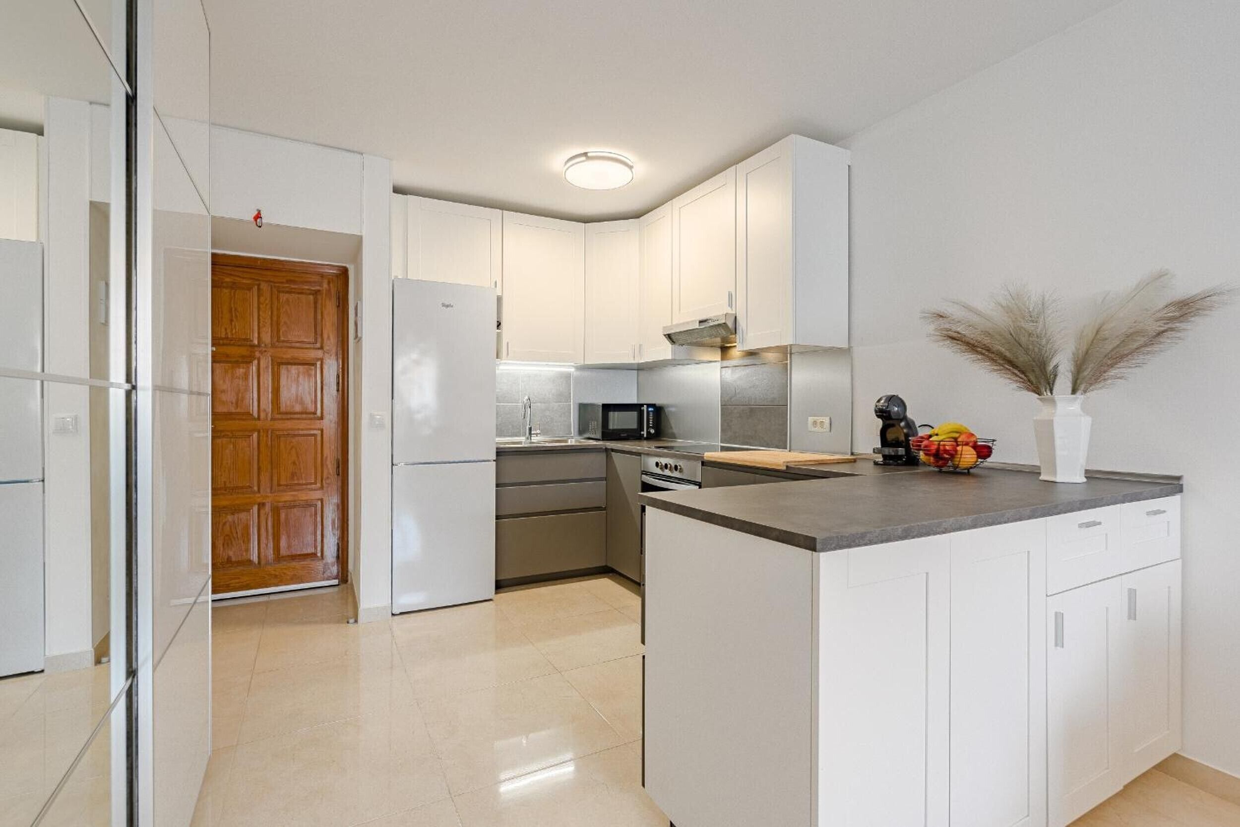 A modern kitchen with white cabinetry, a central island, and a wooden door.