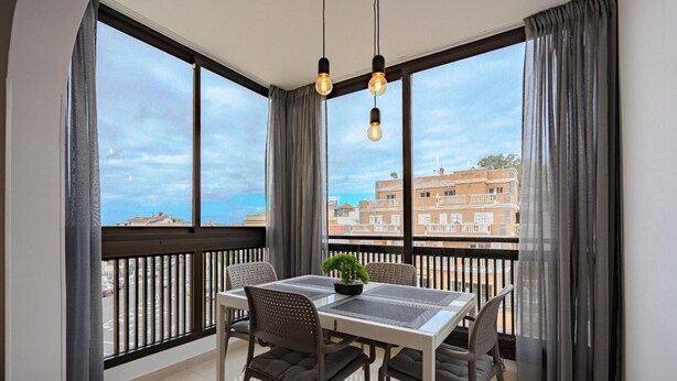 A balcony with a dining table, chairs, a potted plant, and a view of buildings.
