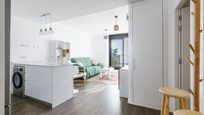 Eine moderne Küche mit Waschmaschine, einem Essbereich mit einem grünen Sofa und einem hölzernen Hocker.
