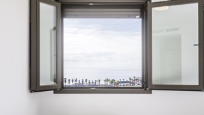 Ein Zimmer mit großem Fenster und Blick auf einen Strand mit Palmen und blauem Himmel.