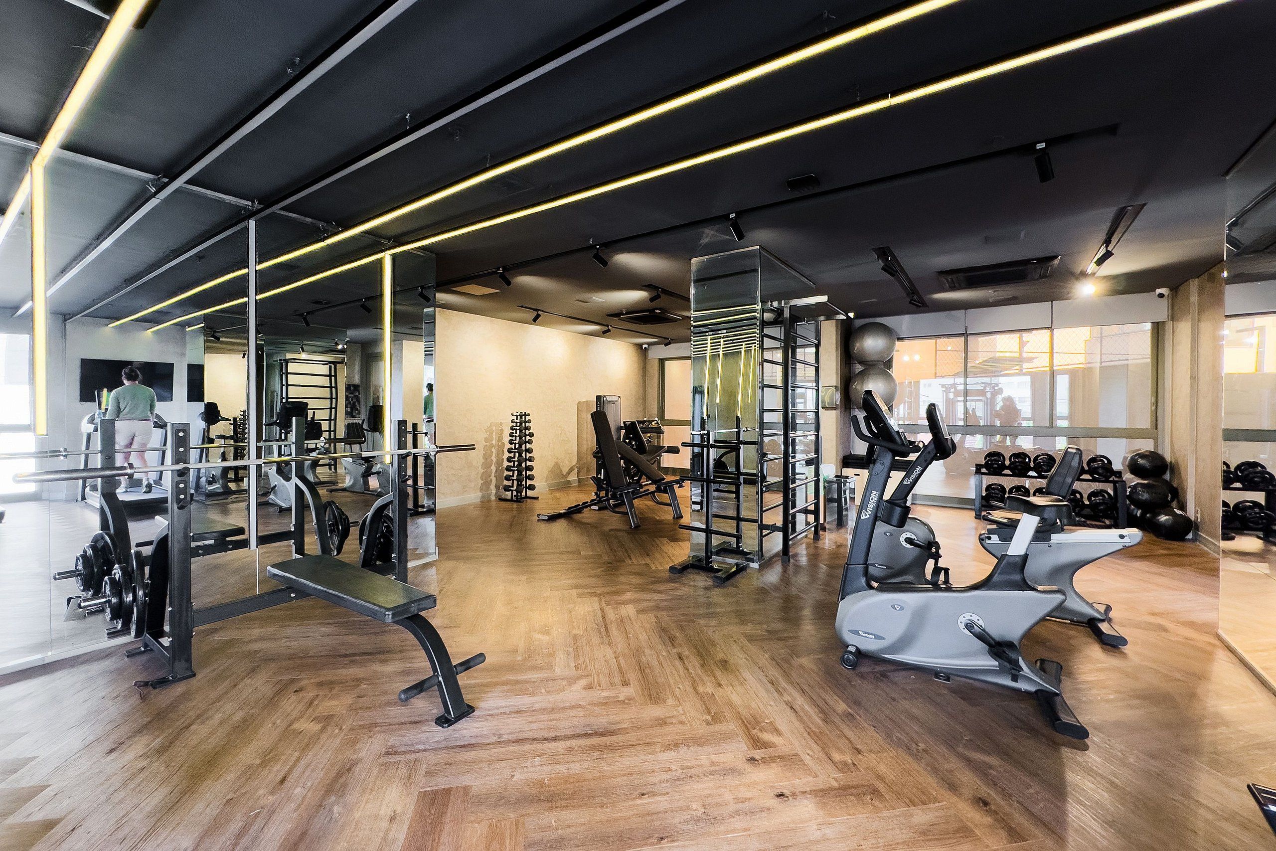 Un gimnasio moderno con suelo de madera, diverso equipo de ejercicio y espejos en las paredes.