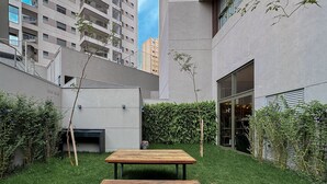 Une terrasse extérieure moderne, avec une table et un banc en bois, entourée d’une haie bien entretenue et d’une pelouse.