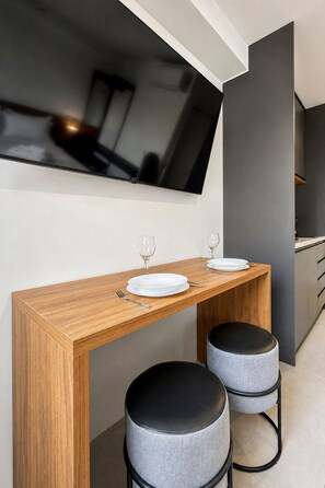 Un espace repas moderne avec une table en bois, deux tabourets gris et un téléviseur fixé au mur.